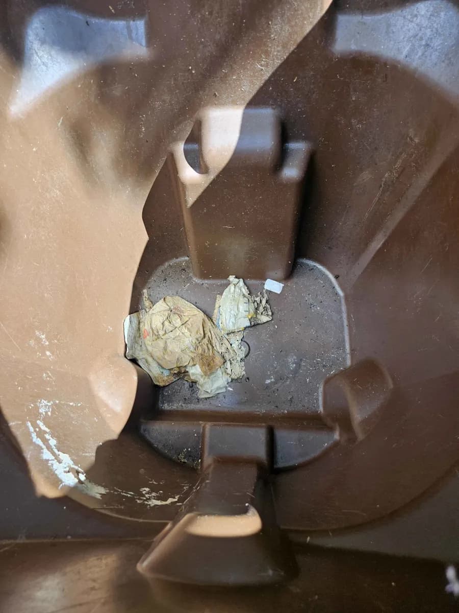 Inside a brown trash bin before cleaning, with old wrappers and grime stuck to the bottom